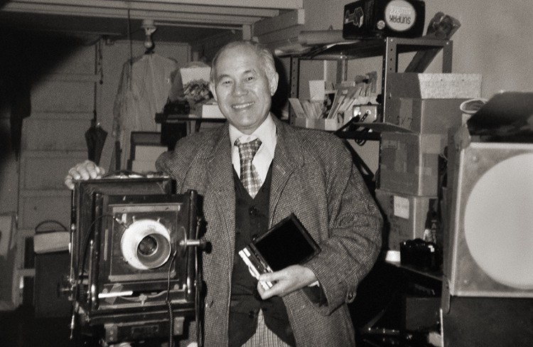 Black and white portrait of Kem Lee posing with a large camera.