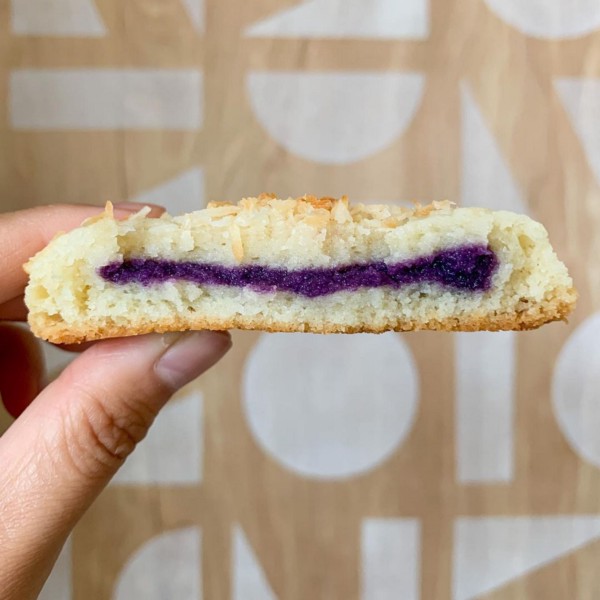A thumb and forefinger hold up a white coconut cookie with purple ube halaya filling.