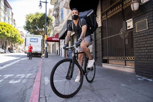 On a city street in San Francisco, a chef balances on his bike while carrying a backpack full of food to be delivered.