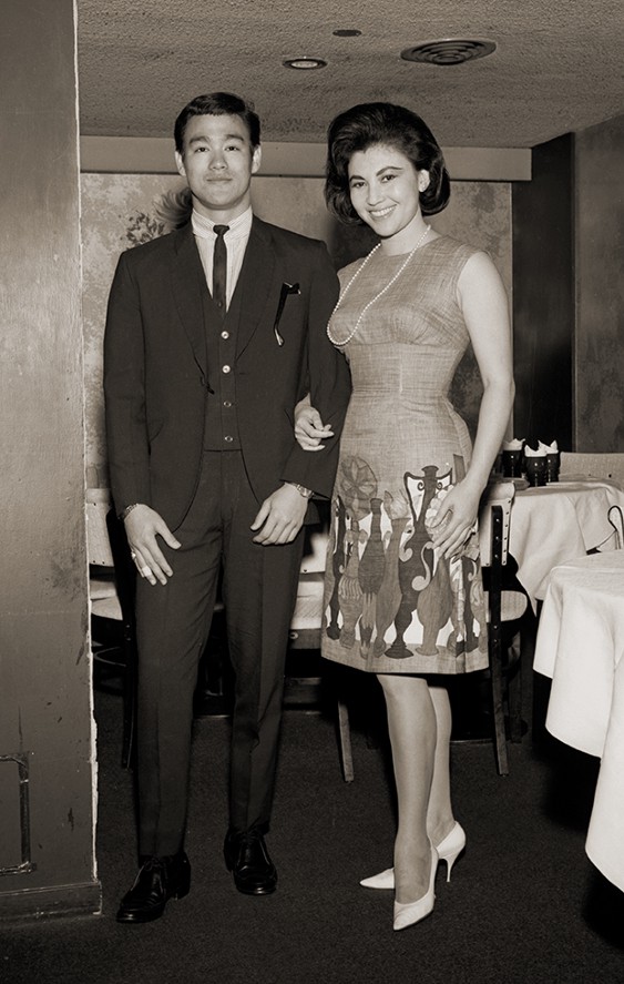 Sepia image of Bruce Lee standing with Diana Chang Chung-Wen in a theatre, dressed in formal attire.