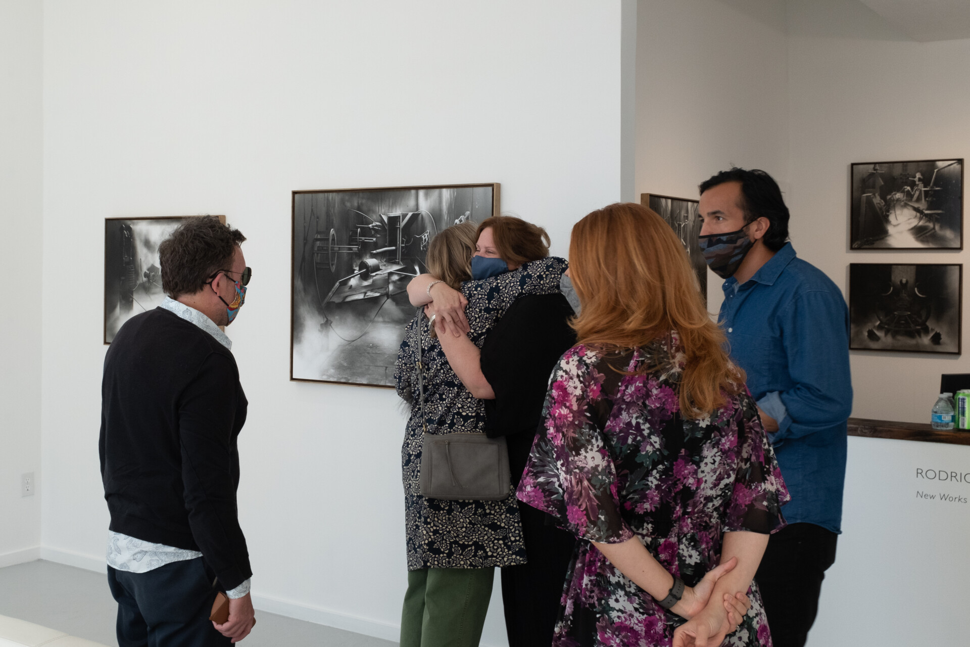 A masked group stands inside an art gallery. Two women hug.