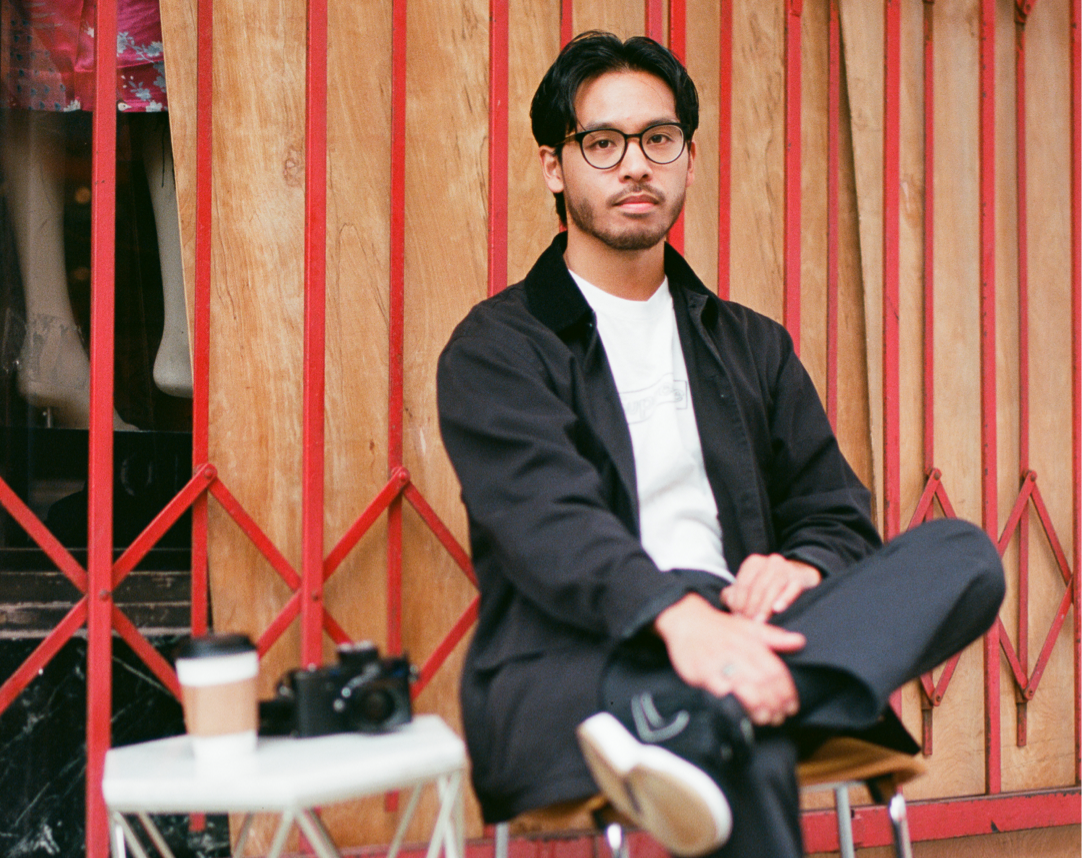 Carlo Velasquez sits at a small table with his camera and a coffee