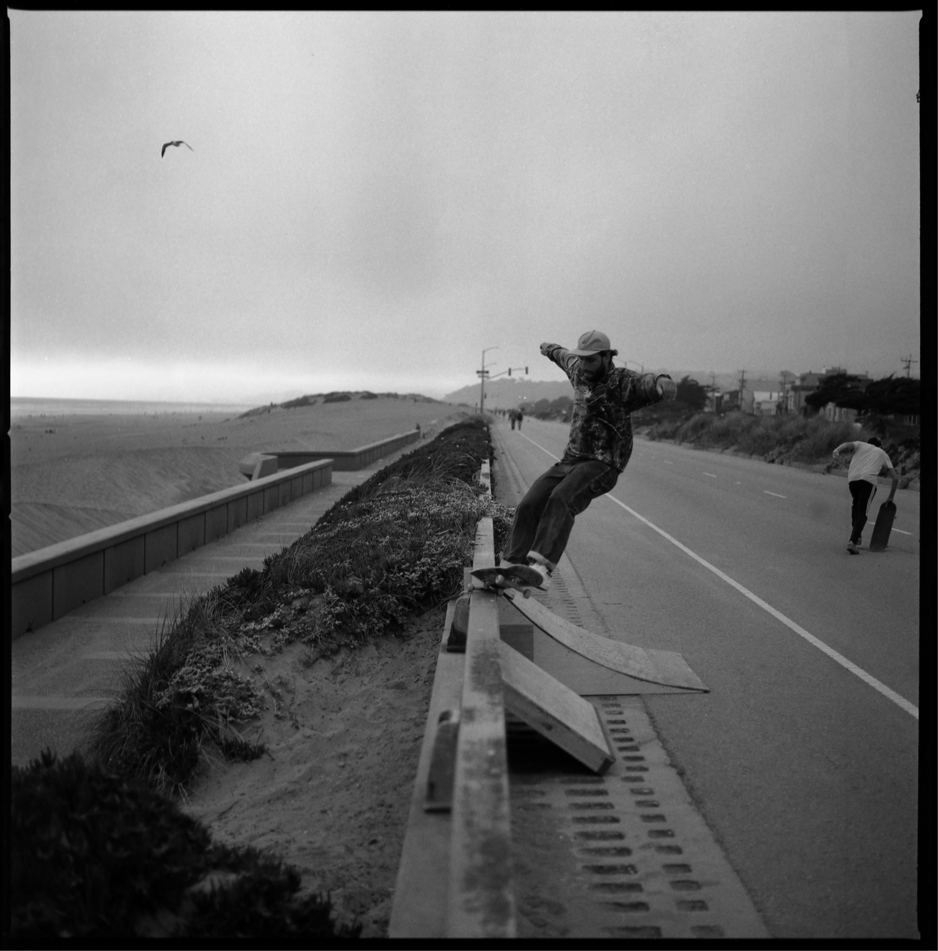 Skateboarder DJ grinds over a three-to-four foot gap from a quarter pipe to the bank on the Great Highway during lockdown in 2020