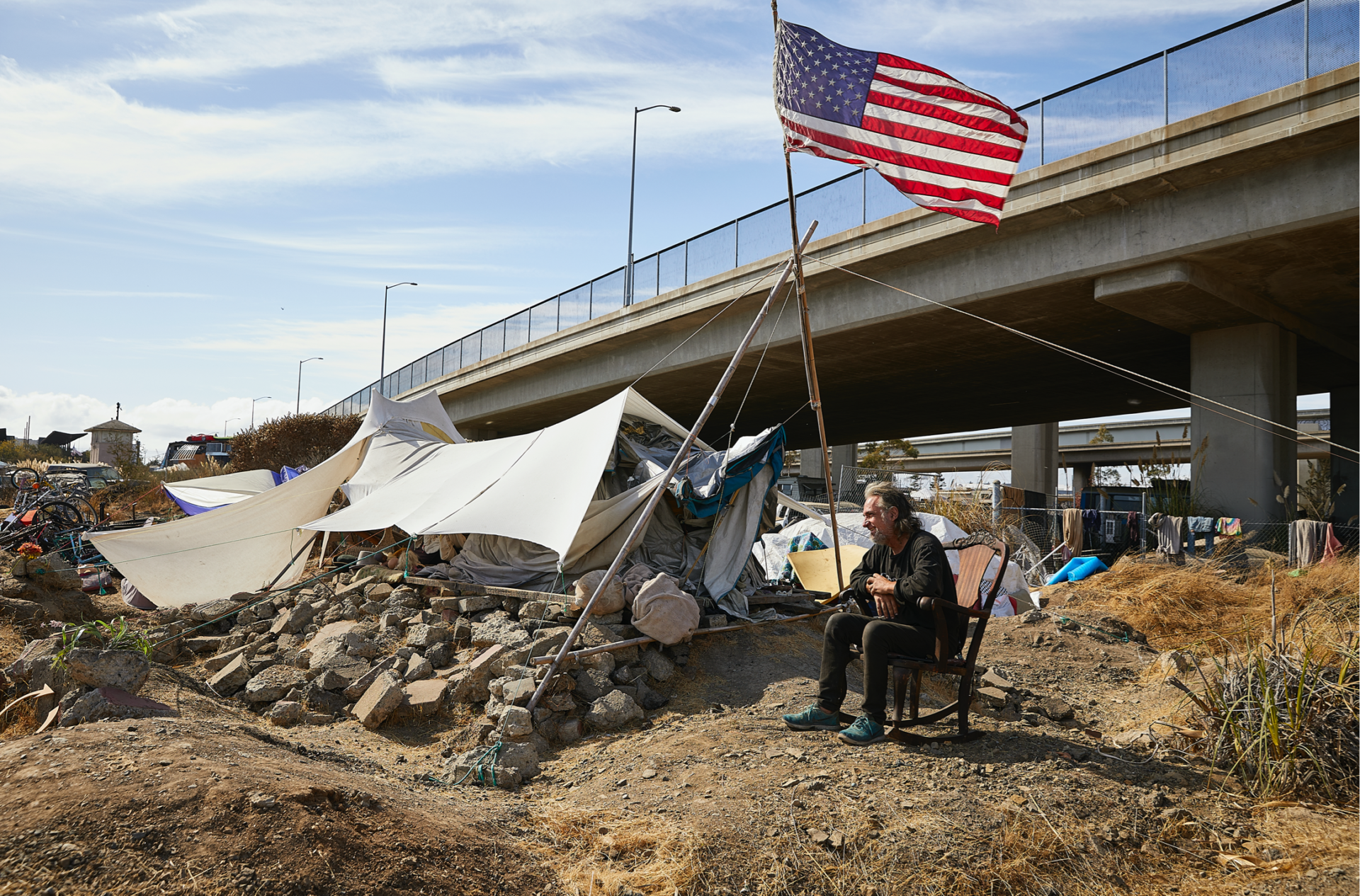 Jones sitting on a chair in front of a tent with an American flag waving above his head