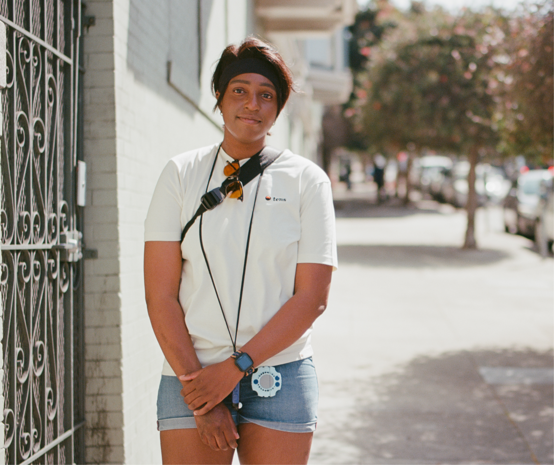 Onome Uyovbievbo (they/them) poses with their camera strapped around their shoulder in the NoPa neighborhood of San Francisco