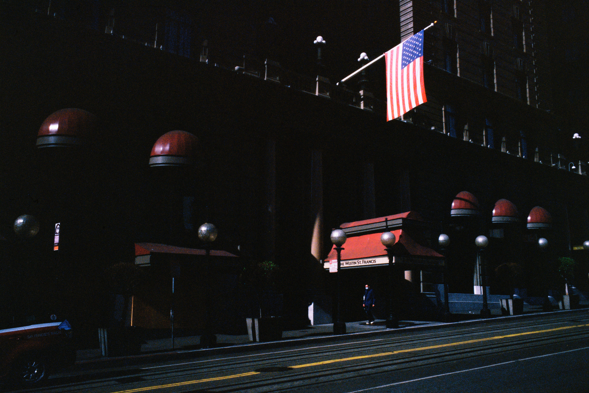 Photograph with harsh lighting of an American flag hovering in front of a hotel over Powell Street