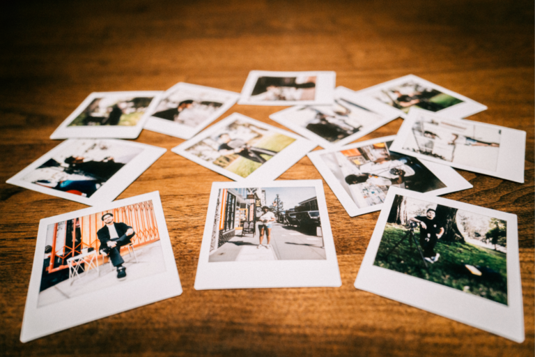 An assortment of polaroids photos laid out on a wooden table from Adam's photo shoots with film photographers Carlo, Onome, and JP