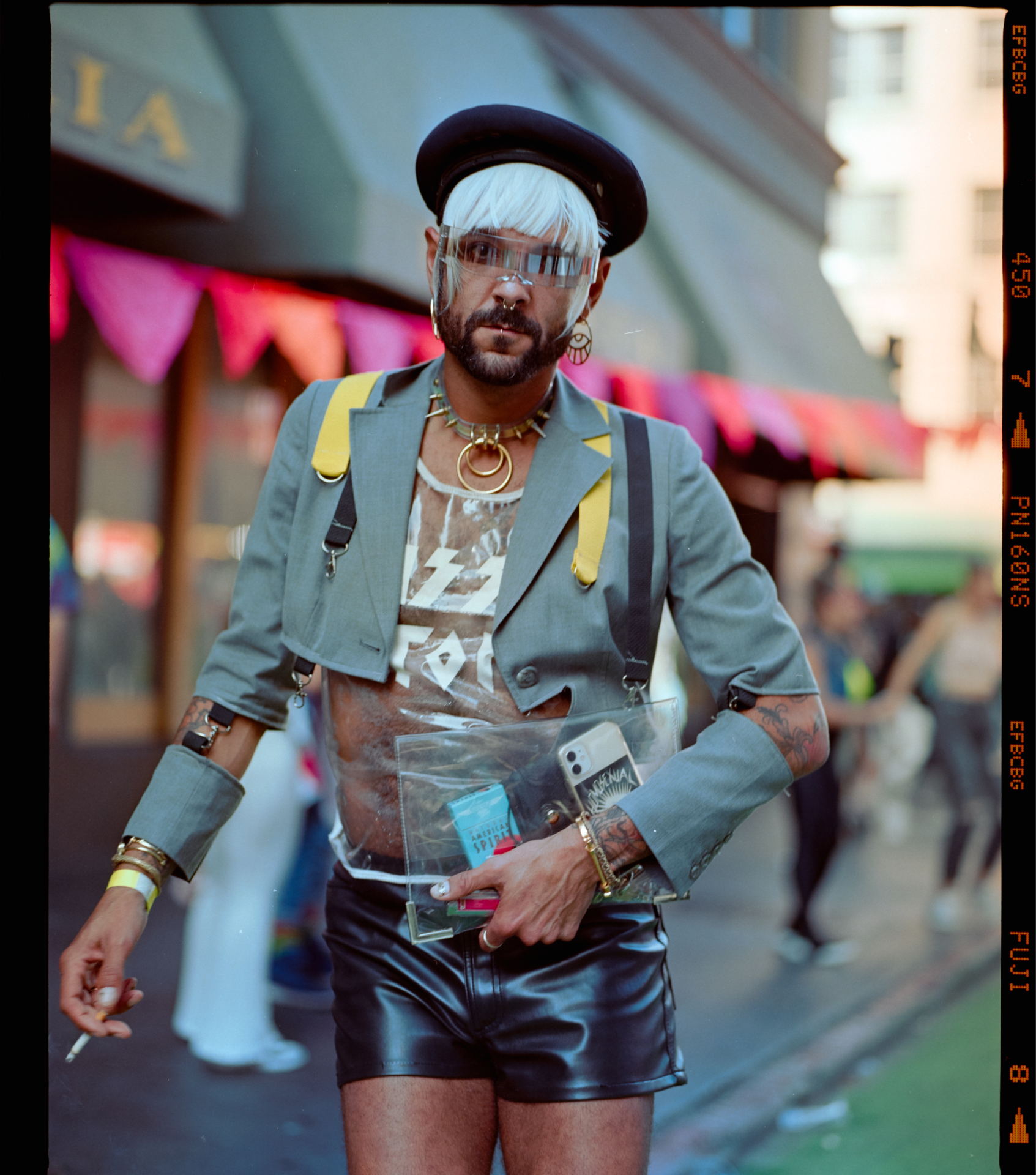 Photograph of Sergio wearing a cut up green blazer on top of a see-through plastic shirt and black leather shorts at the How Weird Street Faire