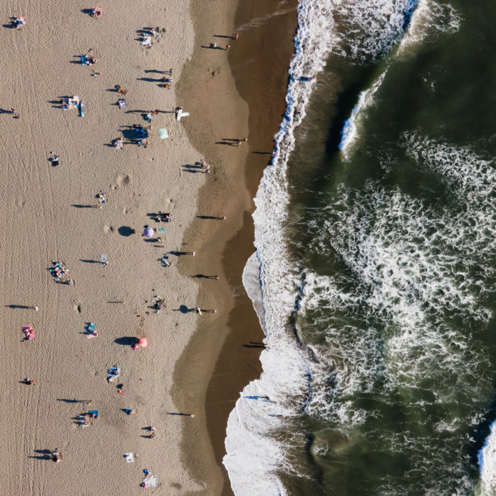 An ominous bird's eye view of waves breaking and encroaching on beachgoers from a dark green body of water