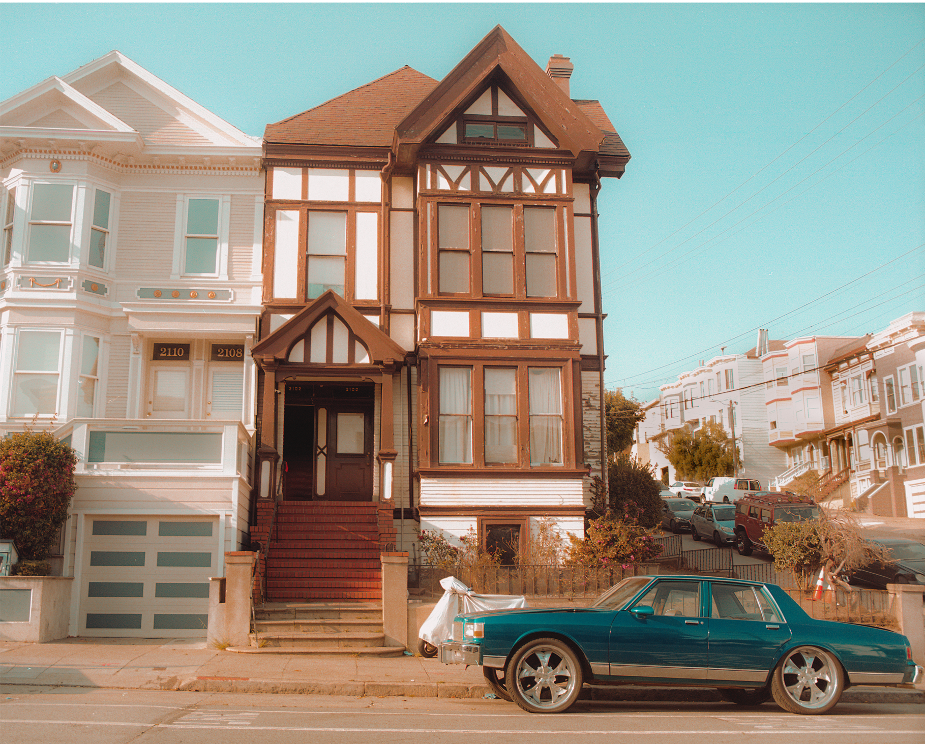 Photograph of a modified blue car parked in front of a typical brown- and white-trimmed Victorian house