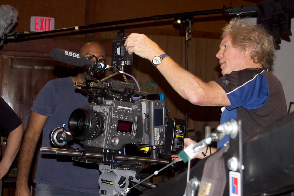 A filmmaker adjusts a large movie camera on set while two team members look on.