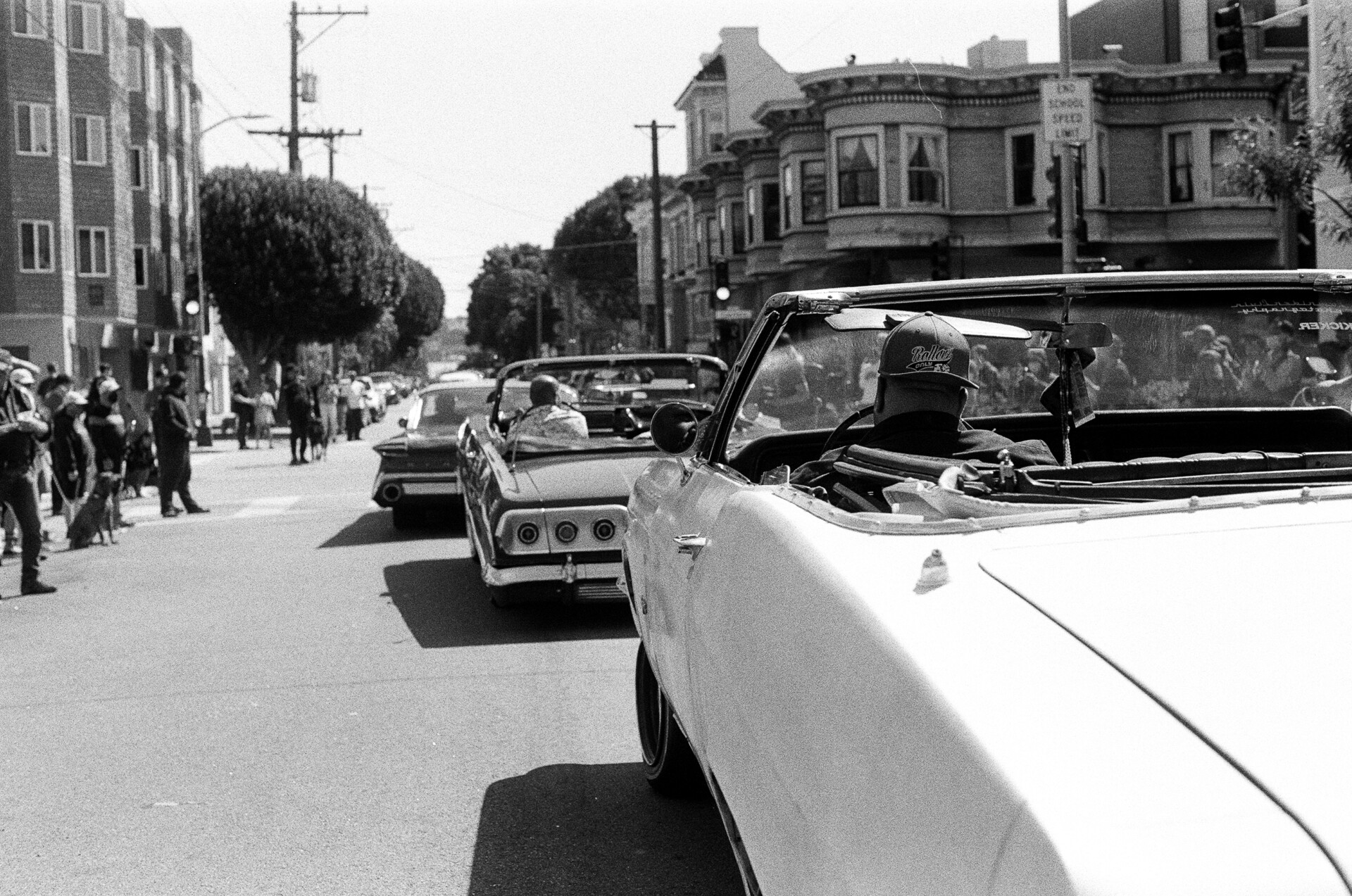 A line of lowrider cars drvie down 19th and Valencia Streets