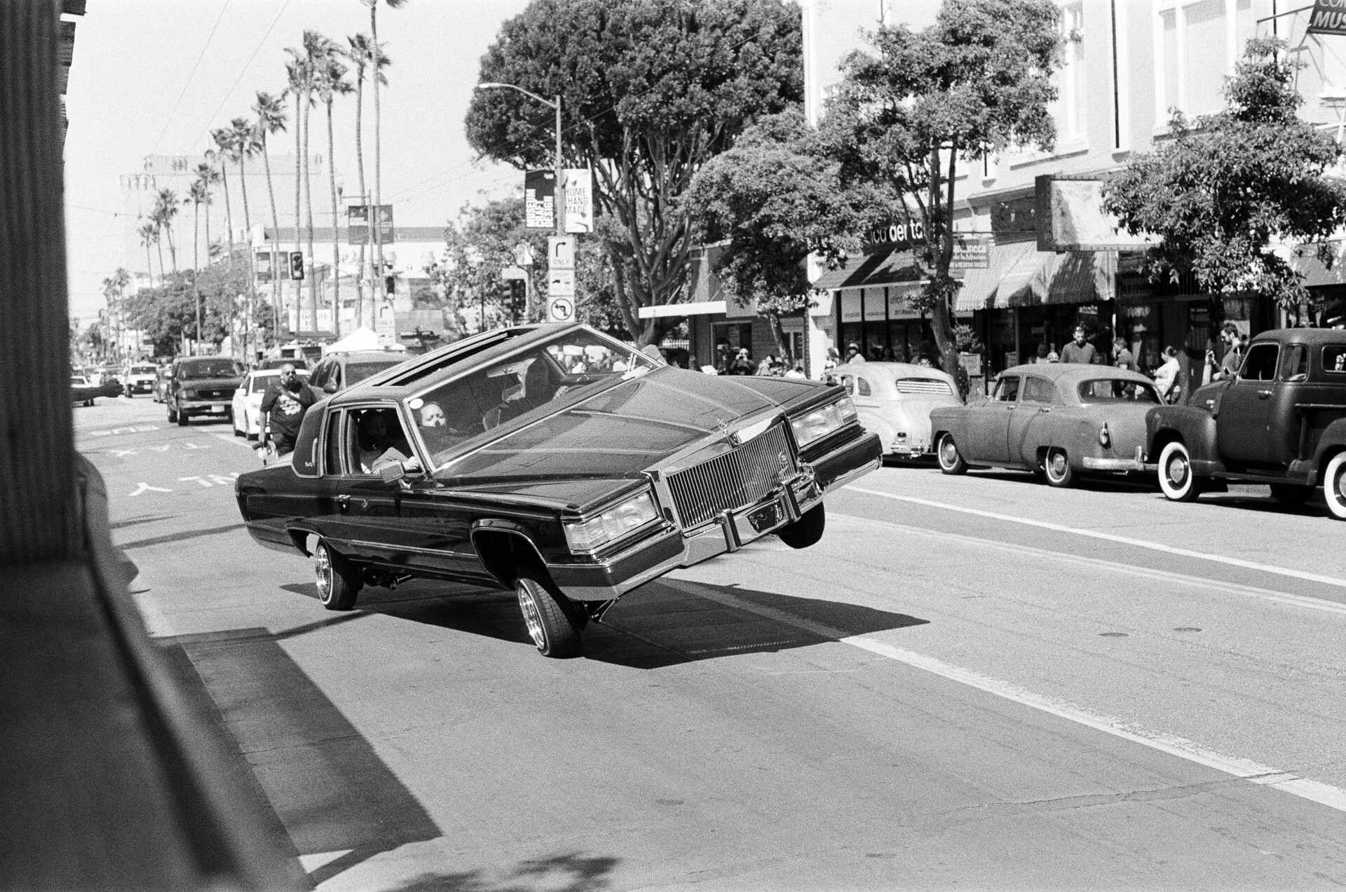 A lowrider shows off the hydraulic suspension capabilities of his car by leaning to the right on Mission Street.